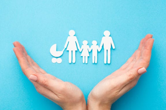 hands splayed out in a caring manner with a paper cutout of a family within to indicate being in good hands