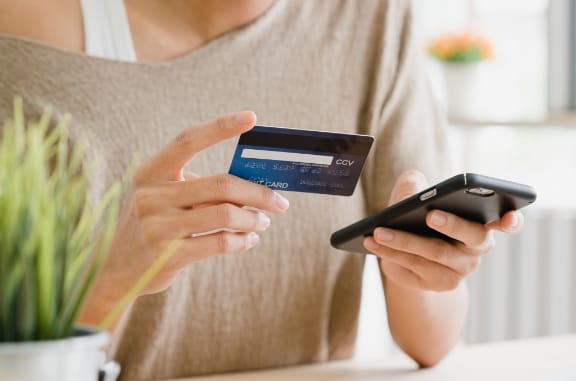 a woman holding her phone in one hand and a credit card in the other indicating she may be making an online payment
